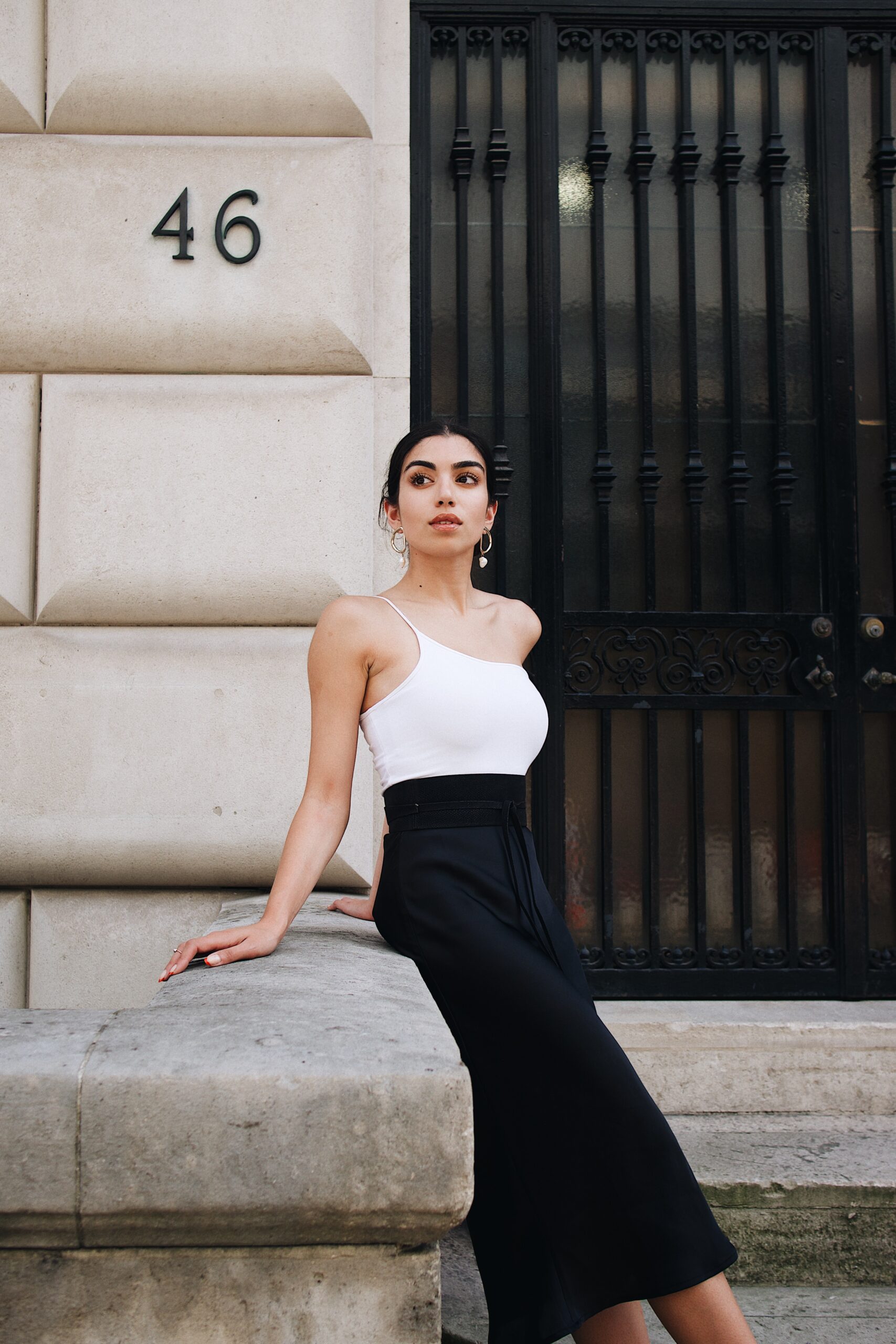 Connie-hiles-Woman in a white camisole and black dress leaning against rail of building entrance-unsplash