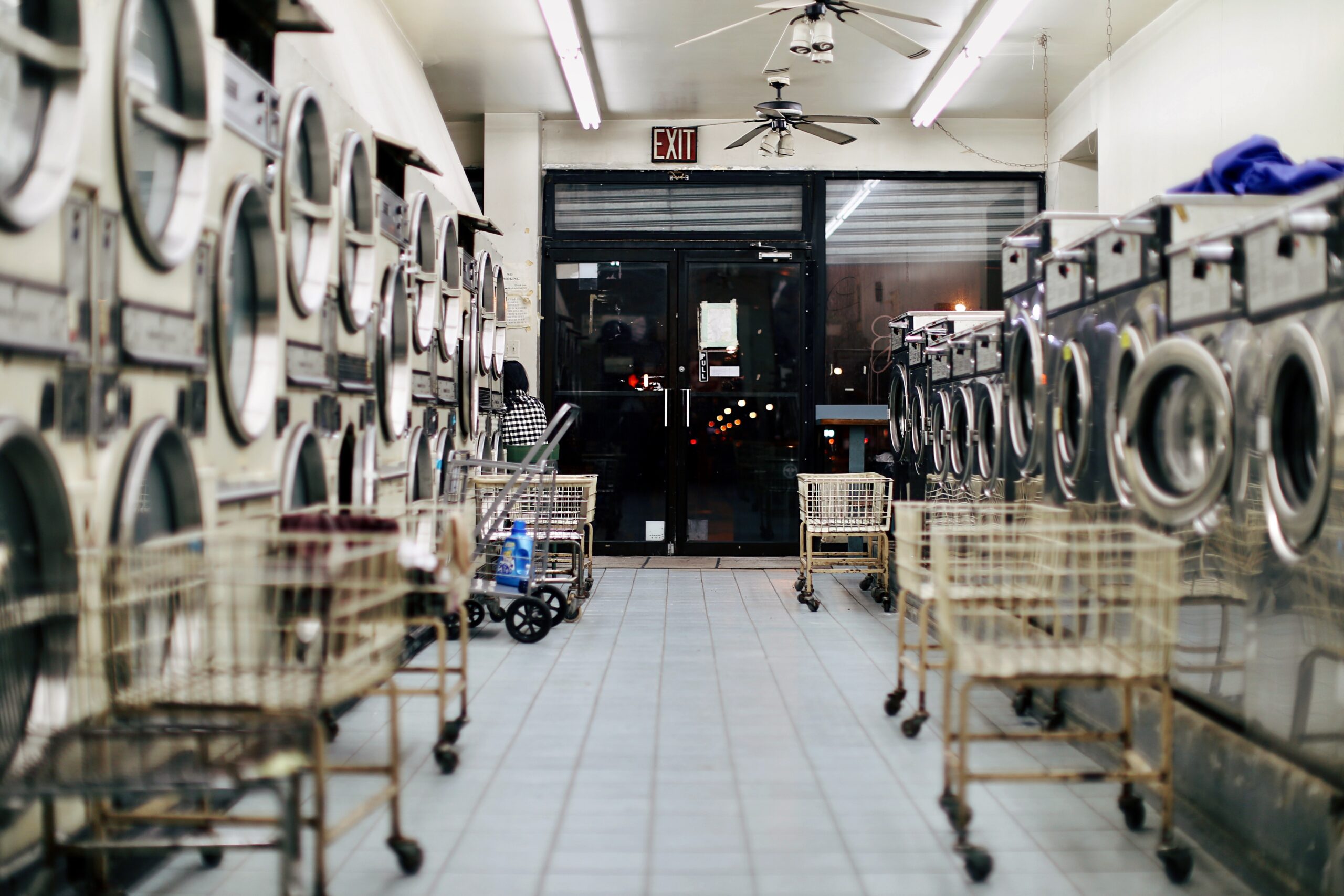 bianca-jordan-Laundry Mat lane with stacked machines on either side and carts lined up against machines-unsplash