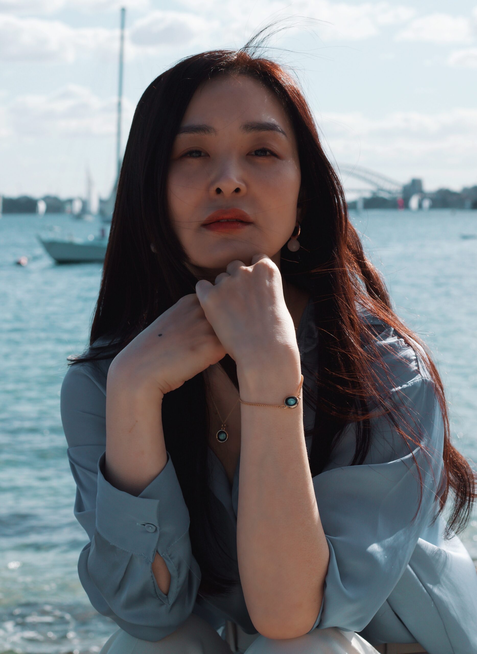 joeyy-lee-Woman sitting at table with ocean background sailboats moored 