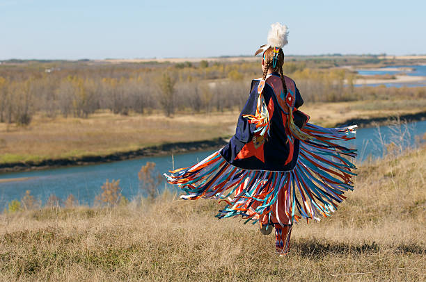 First Nations Women performing a Fancy Shawl Dance in a grass field with a river background